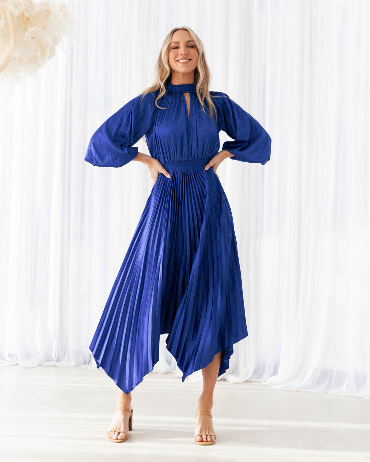 A model is wearing a blue pleated keyhole midi dress with balloon sleeves from the Ebby and I collection designed by Global Fashion House.