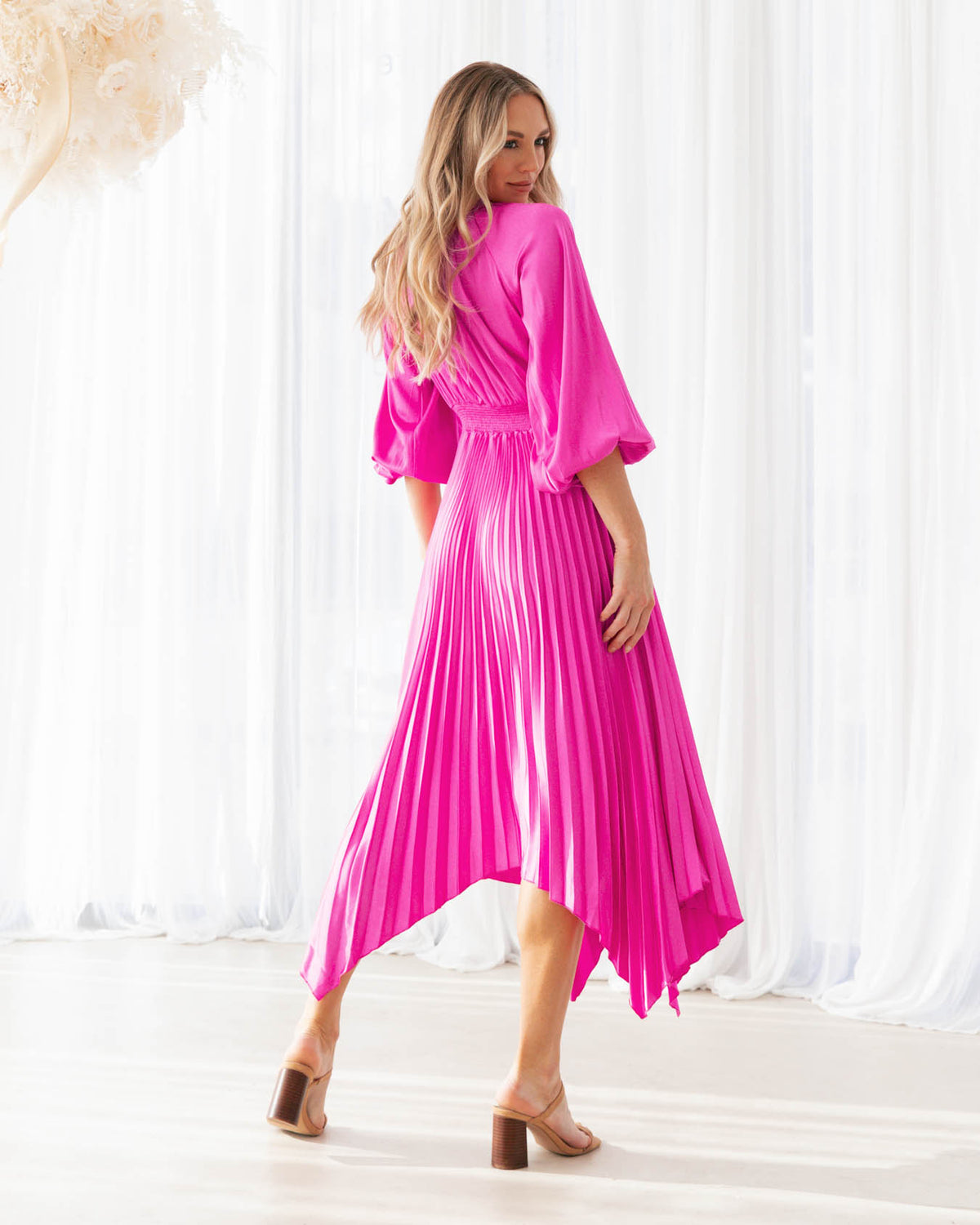A model is wearing a pink pleated keyhole midi dress with balloon sleeves from the Ebby and I collection designed by Global Fashion House.