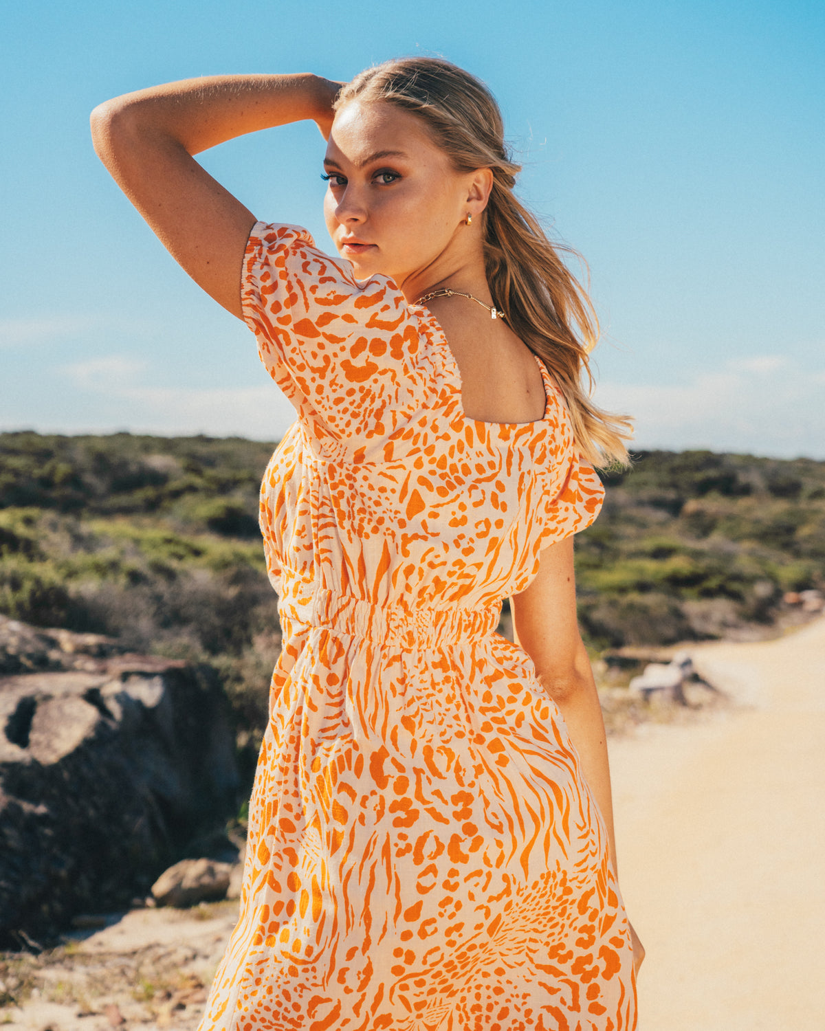 A young woman wearing a linen blend mini dress featuring an exclusive orange animal print, balloon short sleeves, a button-through front, and an elasticated drop shoulder detail designed by Global Fashion House.