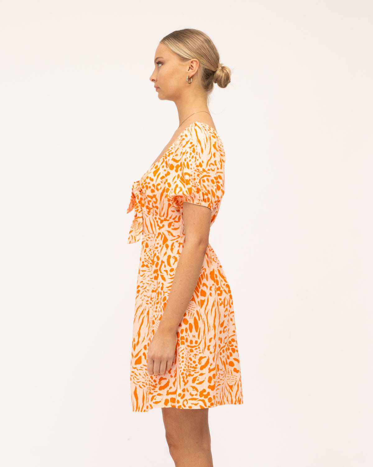 A young woman wearing a linen blend mini dress featuring an exclusive orange animal print, balloon short sleeves, a button-through front, and an elasticated drop shoulder detail designed by Global Fashion House.