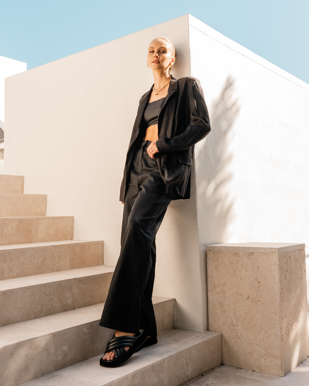 A model is wearing a black cropped top, black trousers, and black linen blazer that&#39;s 100% linen from the White Closet collection designed by Global Fashion House.