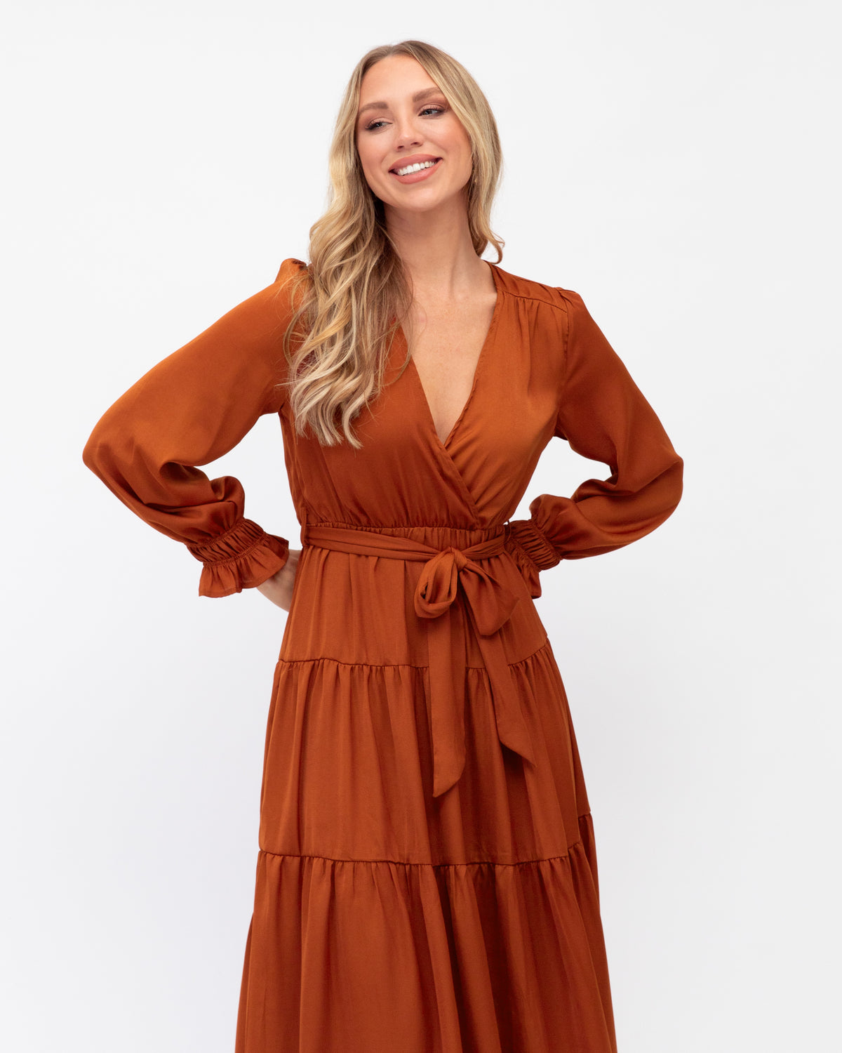 A model wearing a tan tie waist maxi dress that has elasticated cuffs with frill detail and a tiered skirt from the Ebby and I collection designed by Global Fashion House. 