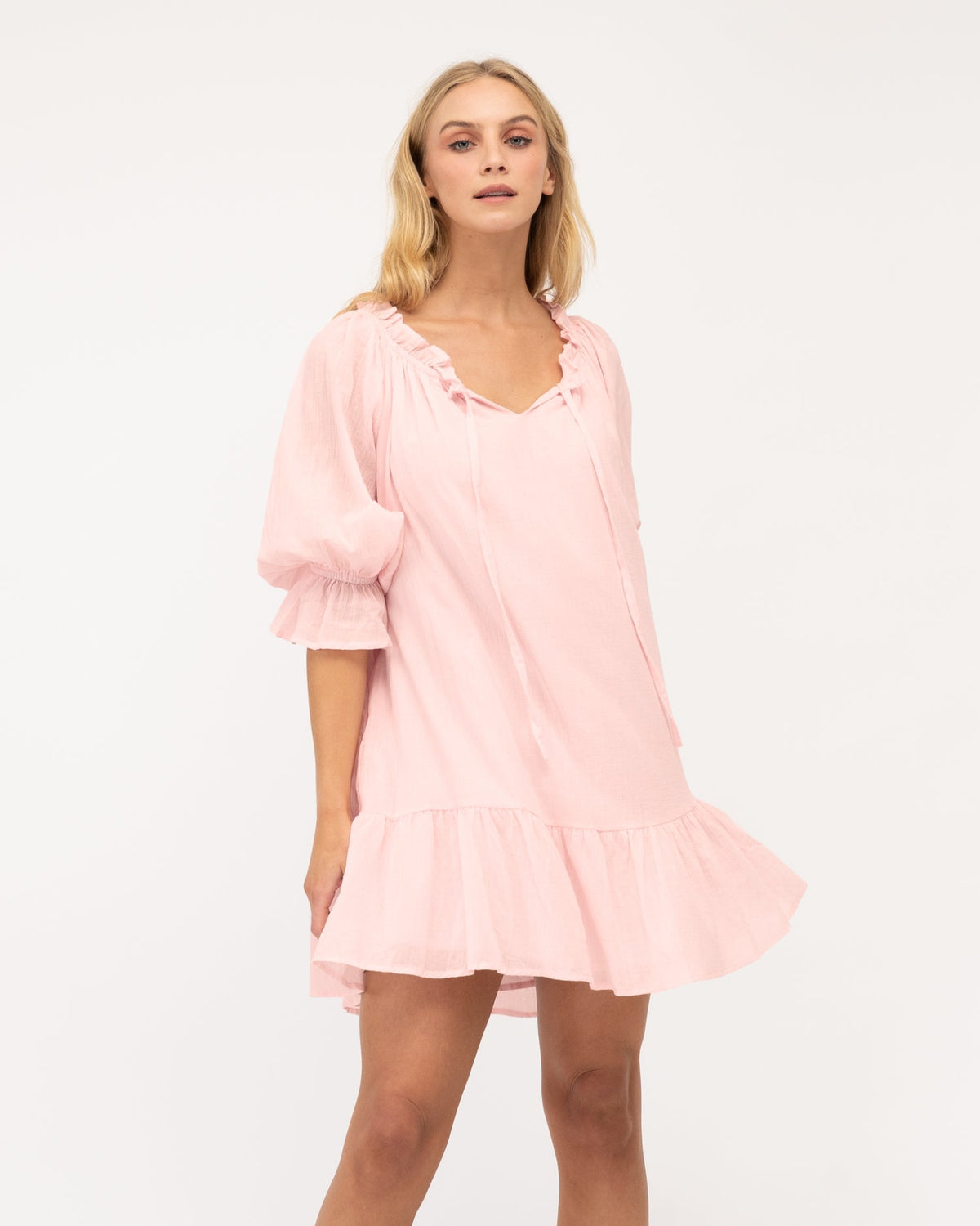 A model wearing a pink ruffle tiered dress and sandals. The dress is fully lined and has a skirt with frill. Pink dress is from the Ebby and I collection designed by Global Fashion House. 