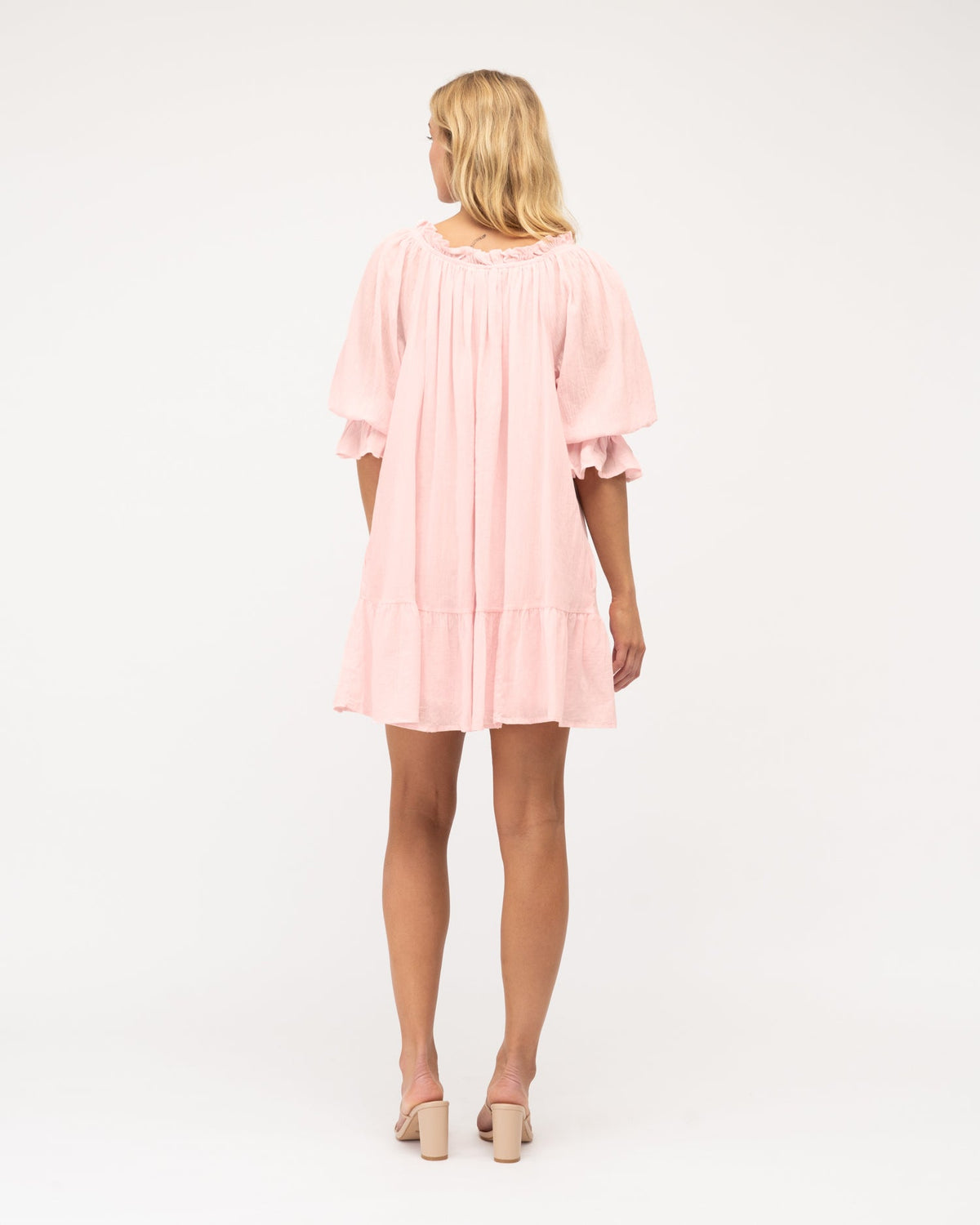 A model wearing a pink ruffle tiered dress and sandals. The dress is fully lined and has a skirt with frill. Pink dress is from the Ebby and I collection designed by Global Fashion House. 