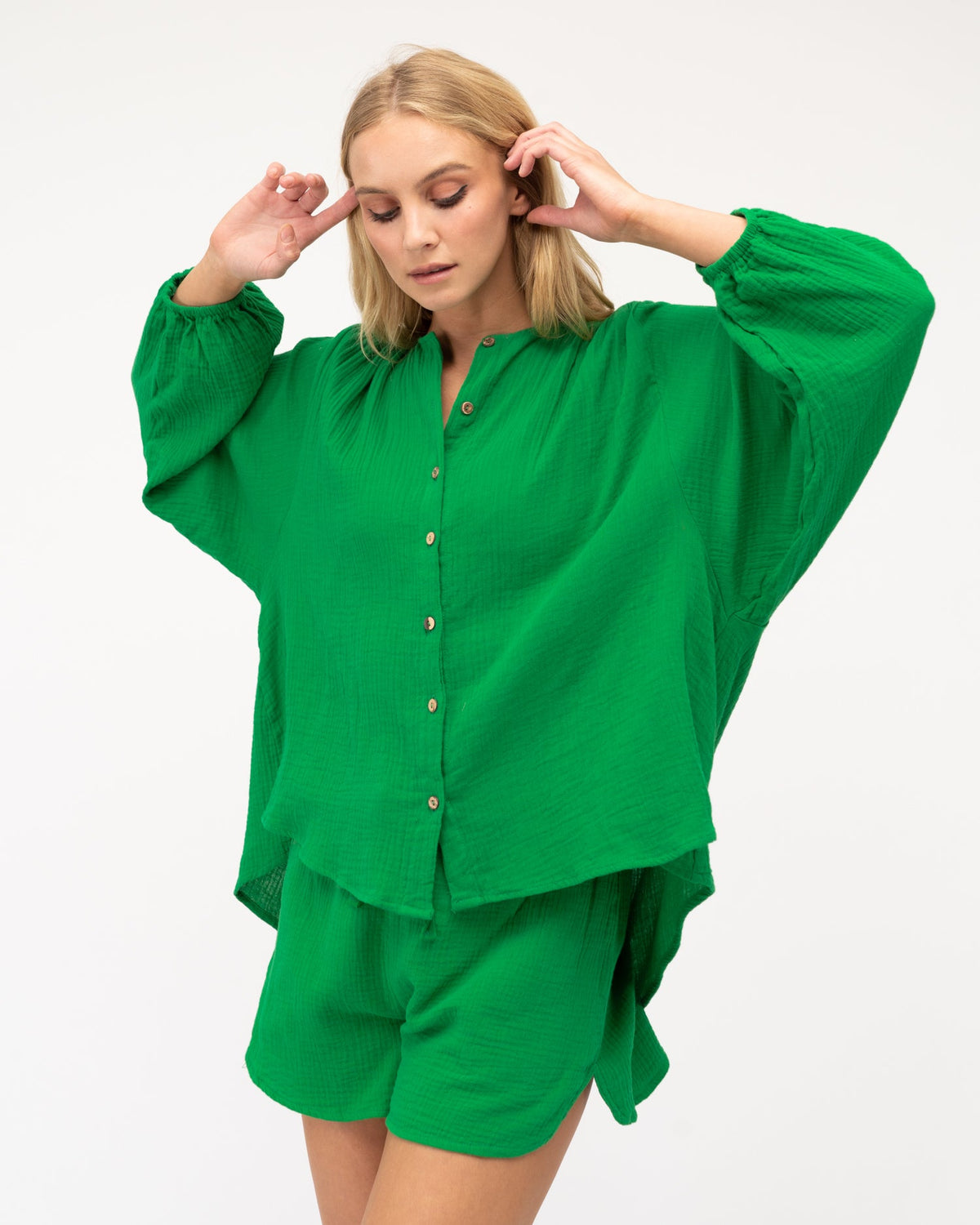 A girl wearing a long sleeve cotton shirt in a bright green colour featuring button-through design with coconut buttons and elasticated cuffs by Global Fashion House.